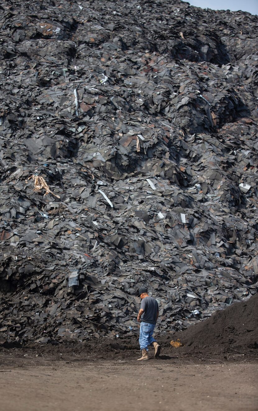 A worker takes a break as a crew begins hauling off the mountain of roofing shingles at Blue...