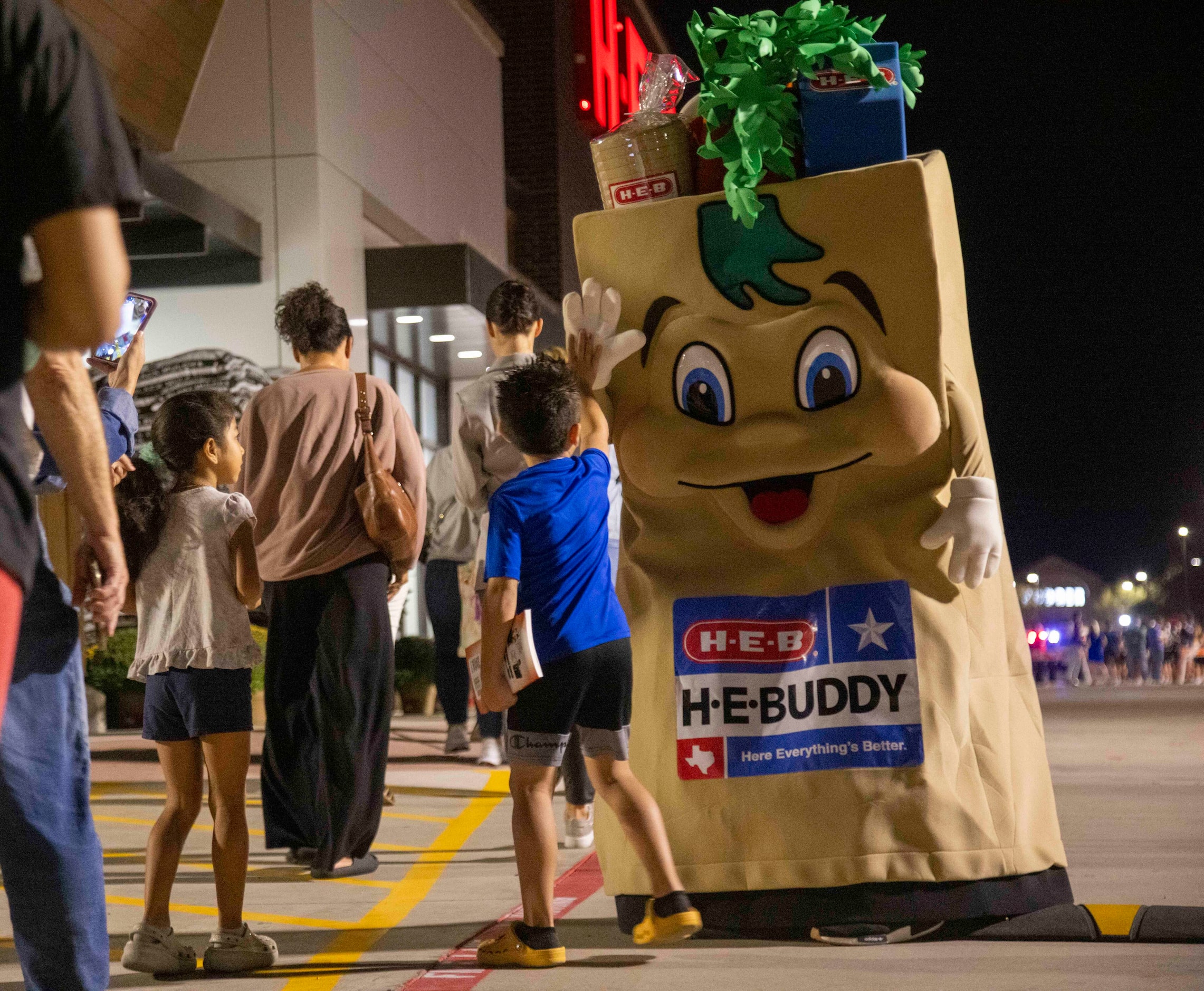 The H-E-Buddy mascot high-fives people waiting in line before the grand opening of the H-E-B...