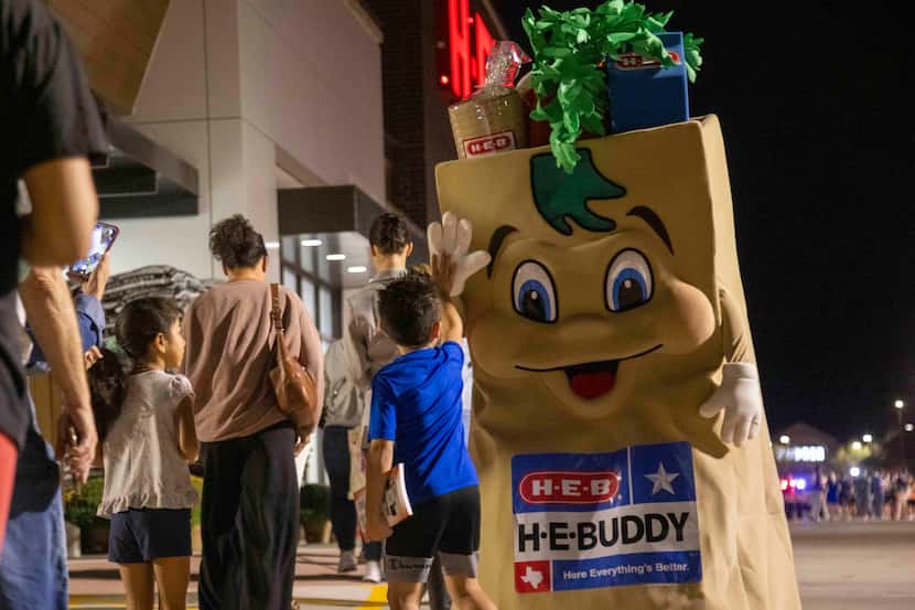 The H-E-Buddy mascot high-fives people waiting in line before the grand opening of the H-E-B...