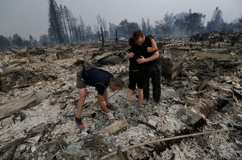 Michael Pond, left, looks through ashes as his wife Kristine, center, gets a hug from Zack...