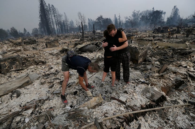 Michael Pond, left, looks through ashes as his wife Kristine, center, gets a hug from Zack...
