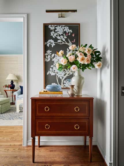 Home's entryway with a small chest topped with flowers and books, with a painting hanging...