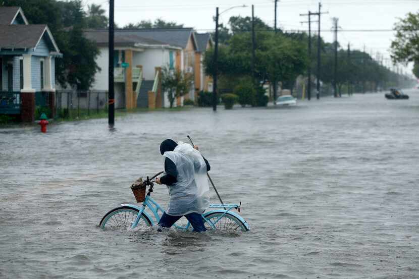 Monica Grant of Galveston pushes her bike through flooded streets near Broadway...