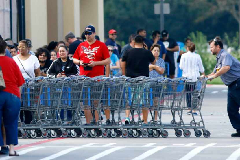 A Wal-Mart employee stacks carts for customers standing in a long line stretched across the...