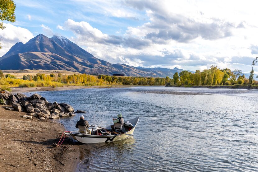 Two people sit in a boat while fishing in Emigrant, MT, with a mountain in the background