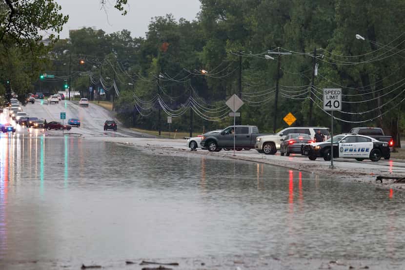 Dallas police officers block traffic as water floods most of Buckner Boulevard near Lake...