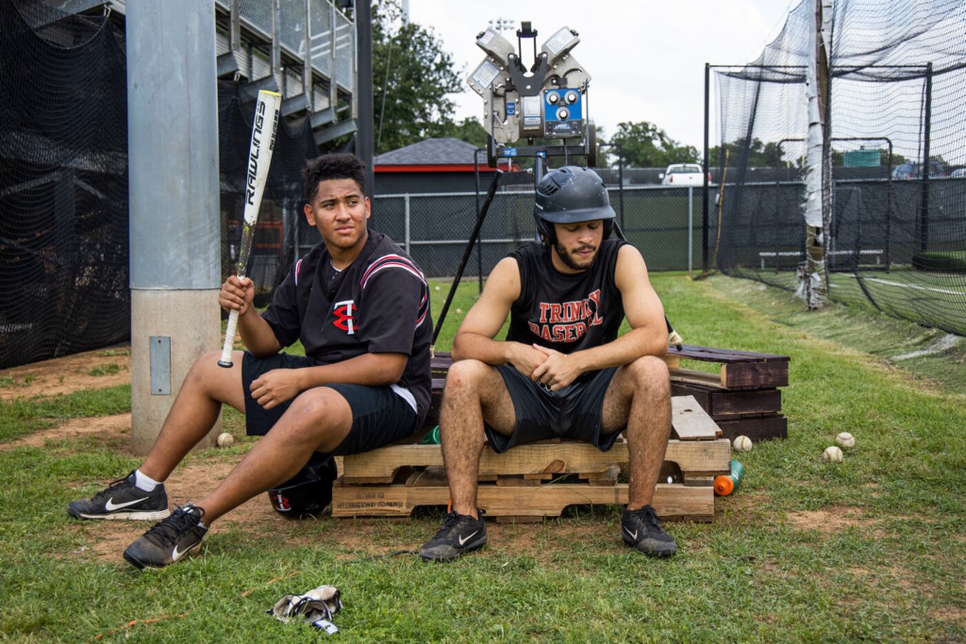 Laki Ellis and Nike Tratree wait their turns in the batting cage during baseball practice at...