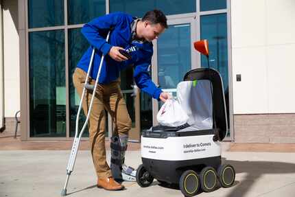 
Garrett Virgin recibe comida de uno de los robots de Starship Technologies, en el campus de...