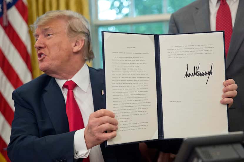 President Donald Trump holds up the executive order he signed to end family separations at...