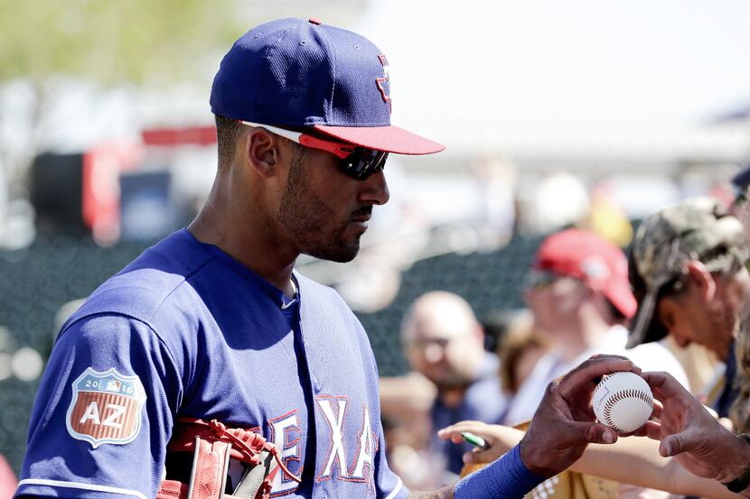 Texas Rangers' Ian Desmond signs autographs before a spring training baseball game against...