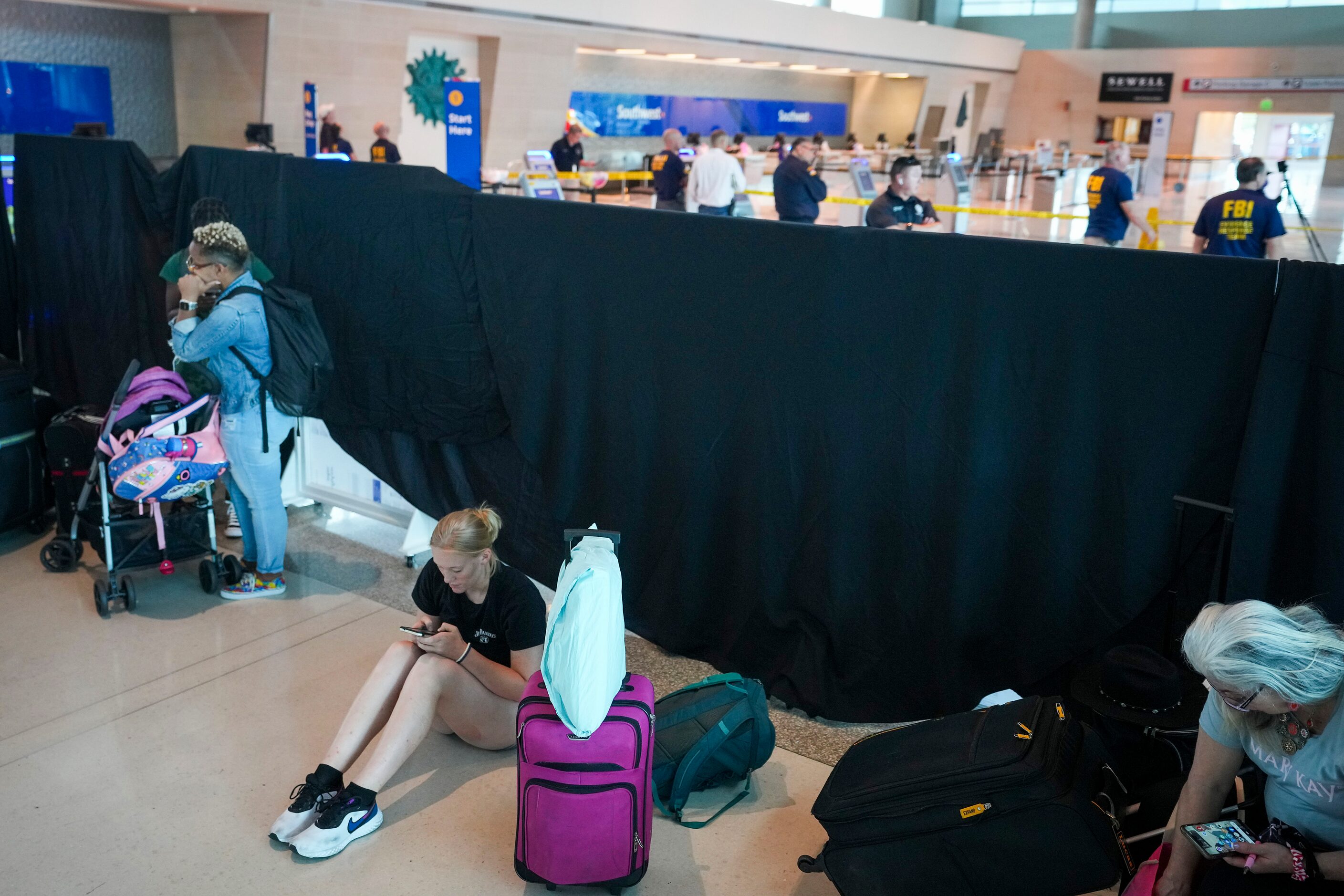 Passengers wait near a curtain separating the Southwest ticket counters from the scene a...