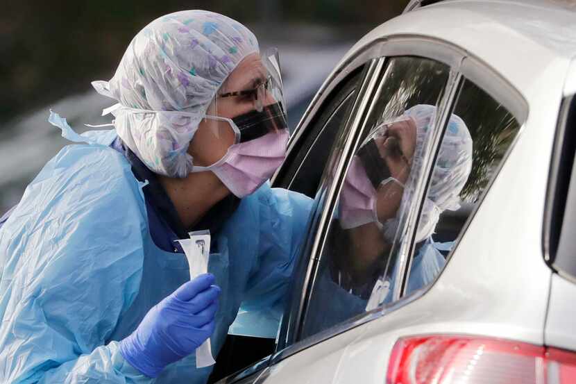 Laurie Kuypers, a registered nurse, reaches into a car to take a nasopharyngeal swab from a...