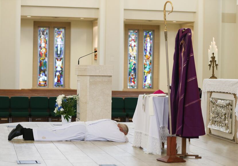 Bishop Edward J. Burns prostrates on the altar as a sign of humility and penance during a...