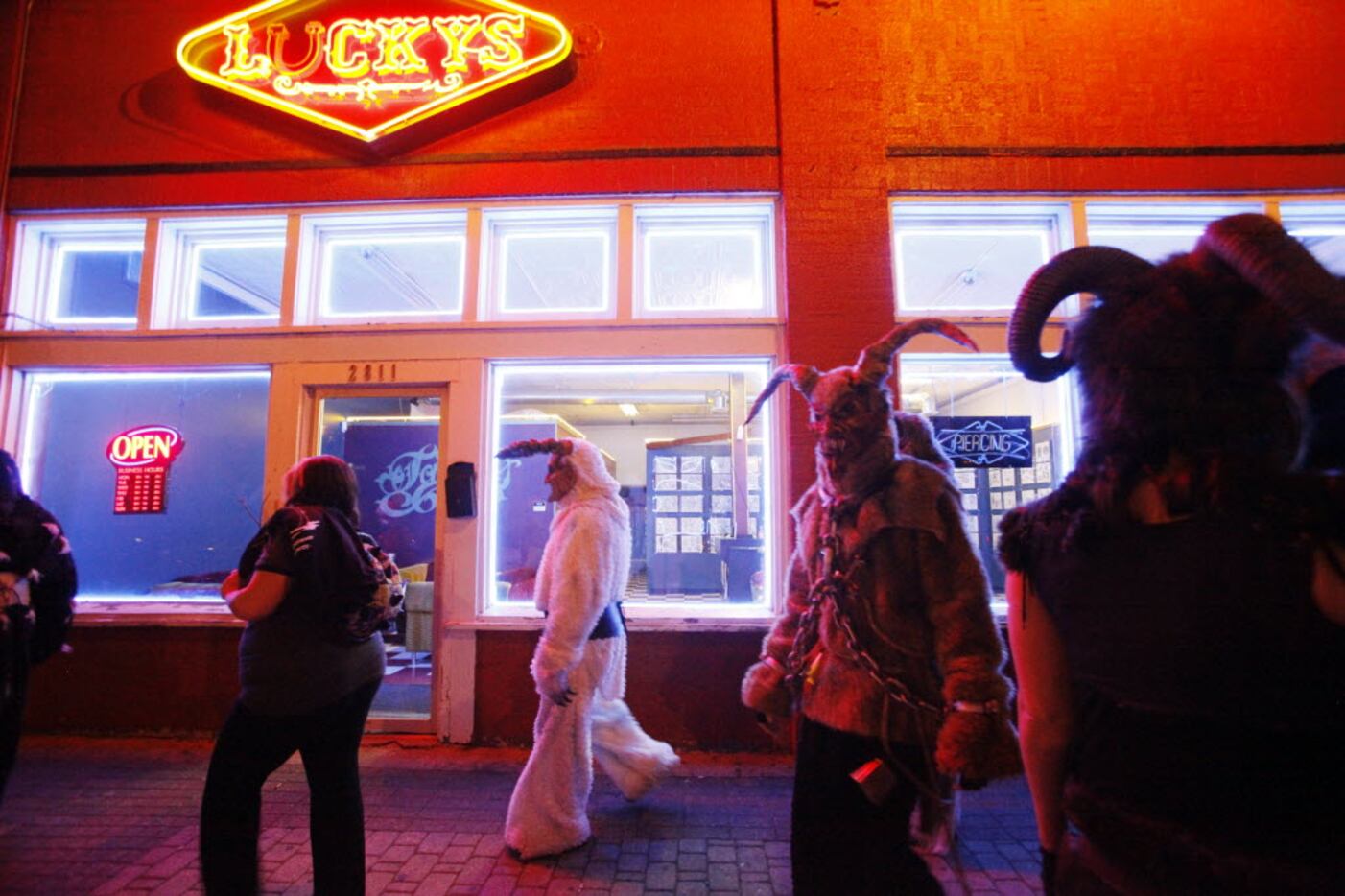 Krampus characters walk passed Lucky's tattoo shop during the Dallas Krampus Walk through...