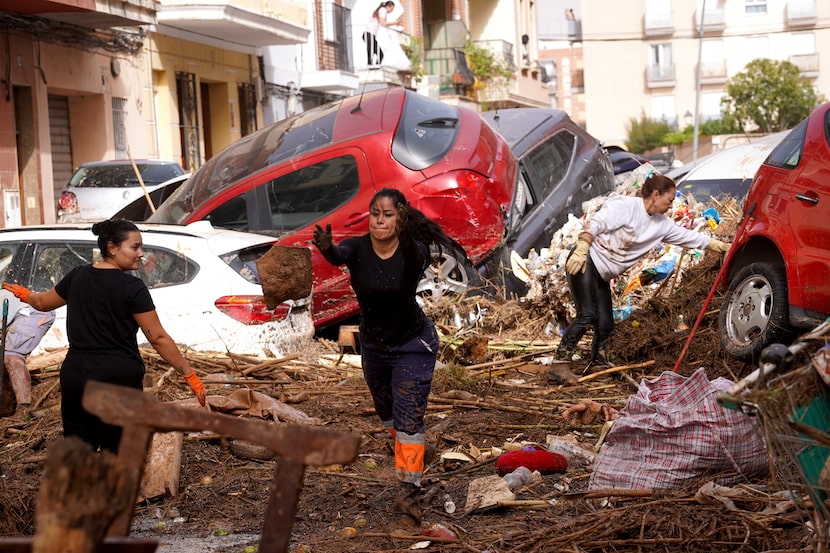 Residents clean the street next to cars piled up after being swept away by floods in...