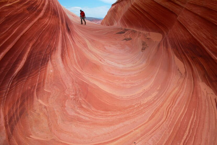 A hiker traverses a rock formation known as The Wave in the Vermilion Cliffs National...