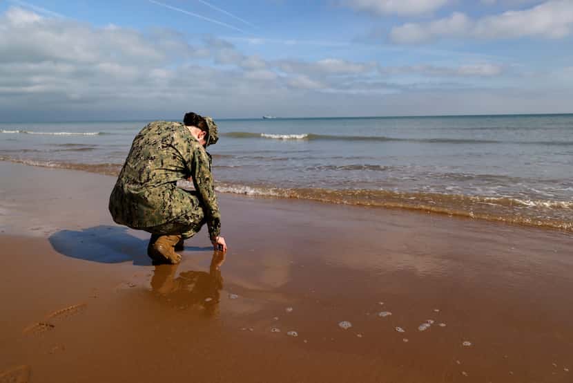 An American soldier touches the sand on Omaha Beach in Normandy, France, on Tuesday, June 4,...