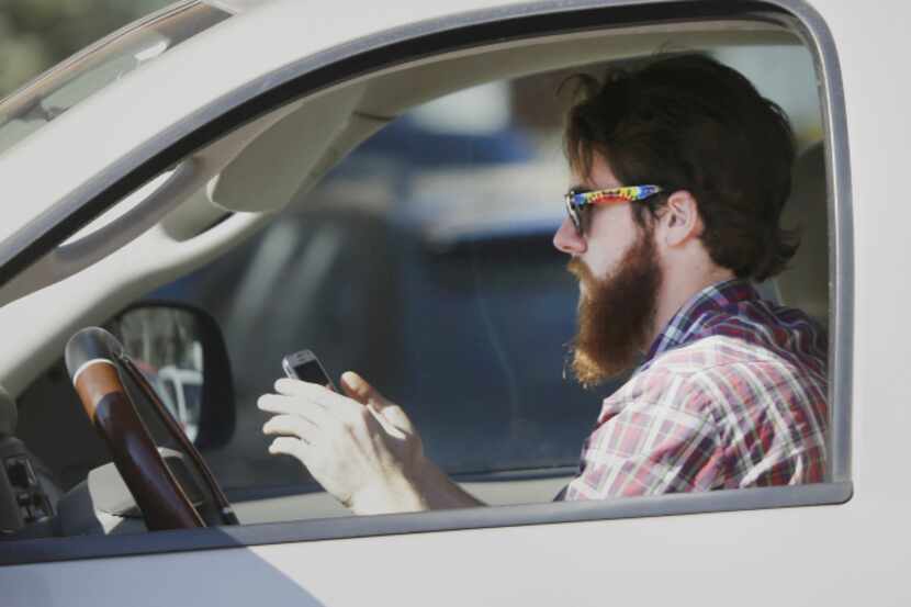 A man works his phone as he drives through traffic in Dallas.