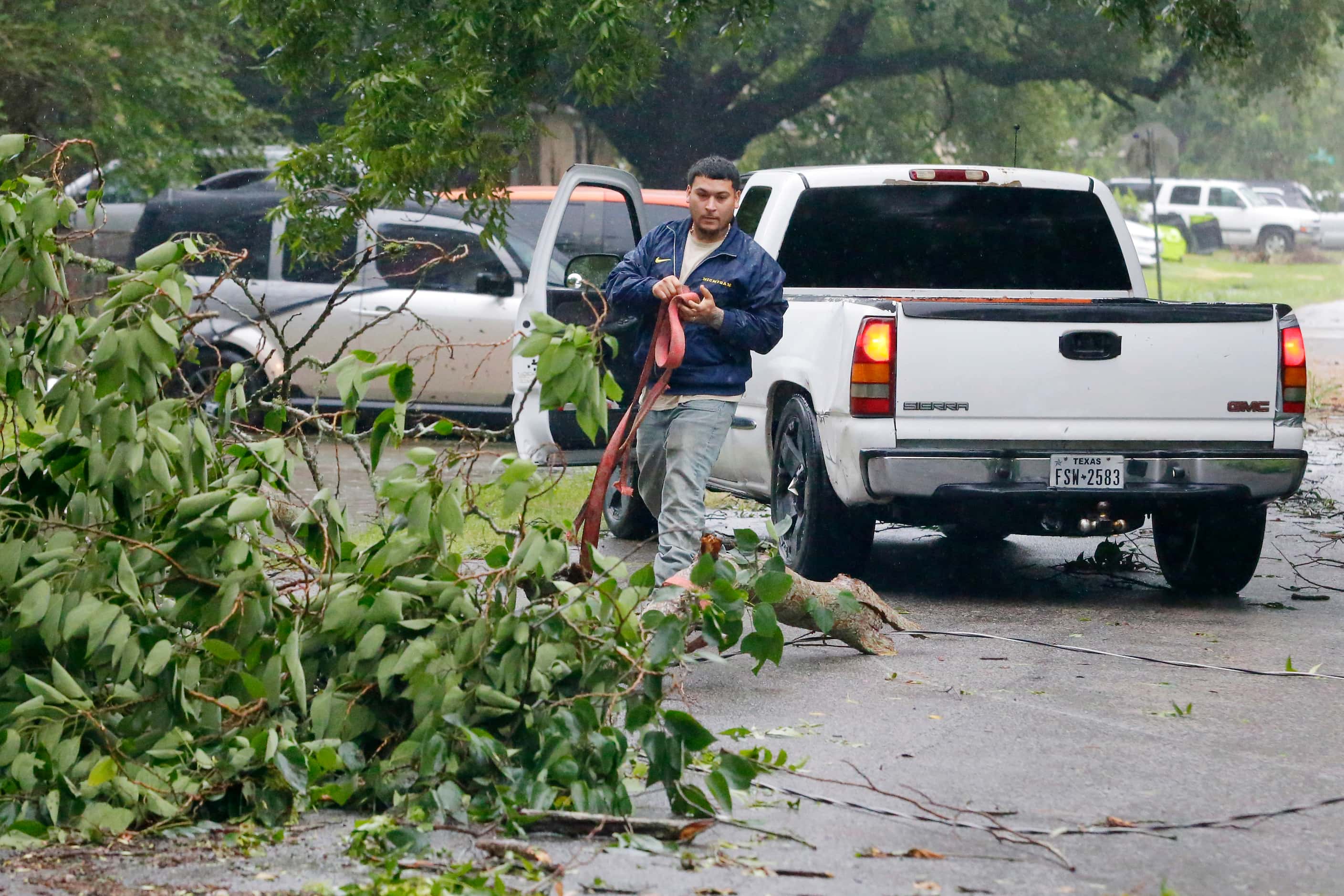 William Ruiz uses a tow strap and his pick-up truck to remove a downed tree branch from the...