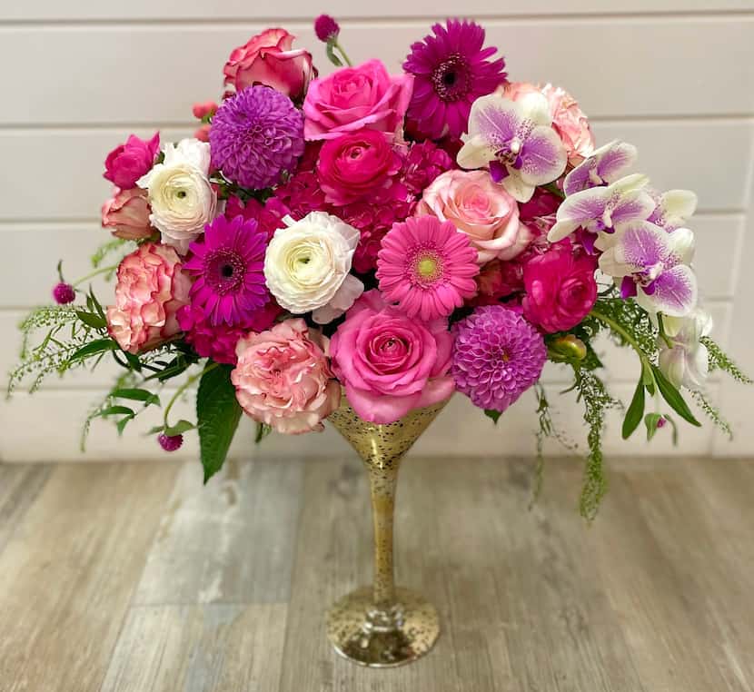 Pink and purple bouquet of roses in a gold martini glass against a white wall