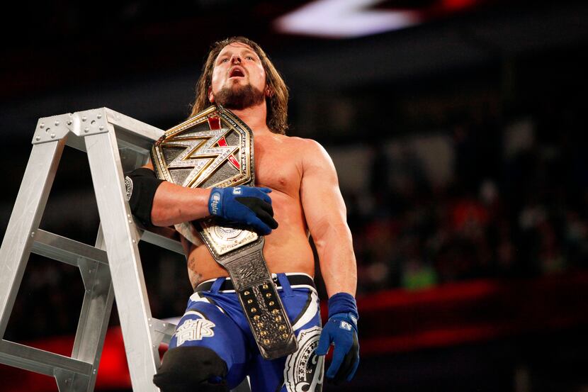 WWE world heavyweight champion AJ Styles reacts with exhaustion as he sits atop a ladder...