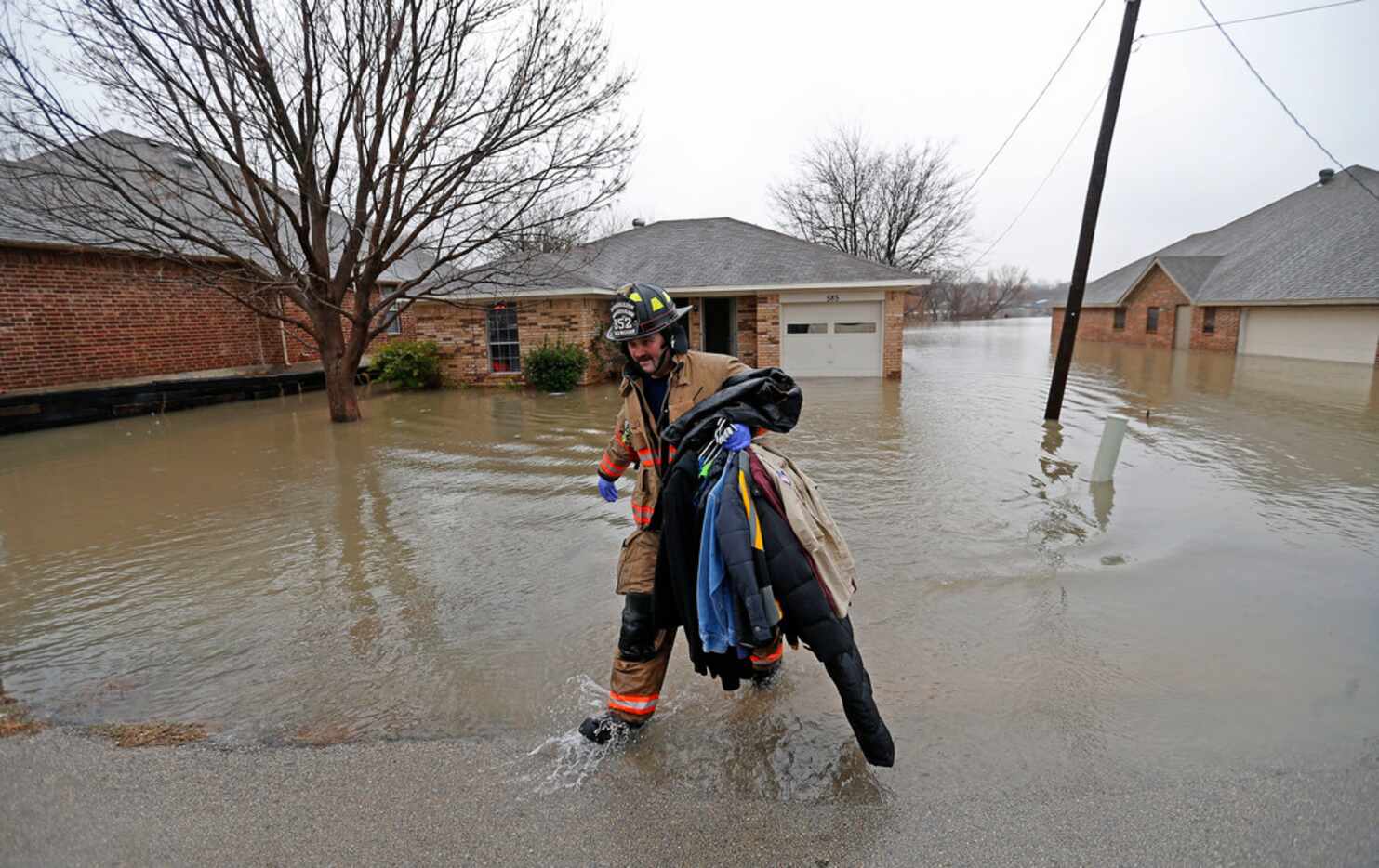 A Rockwall firefighter carries clothing out of the flooded house on Lakeside Drive in...
