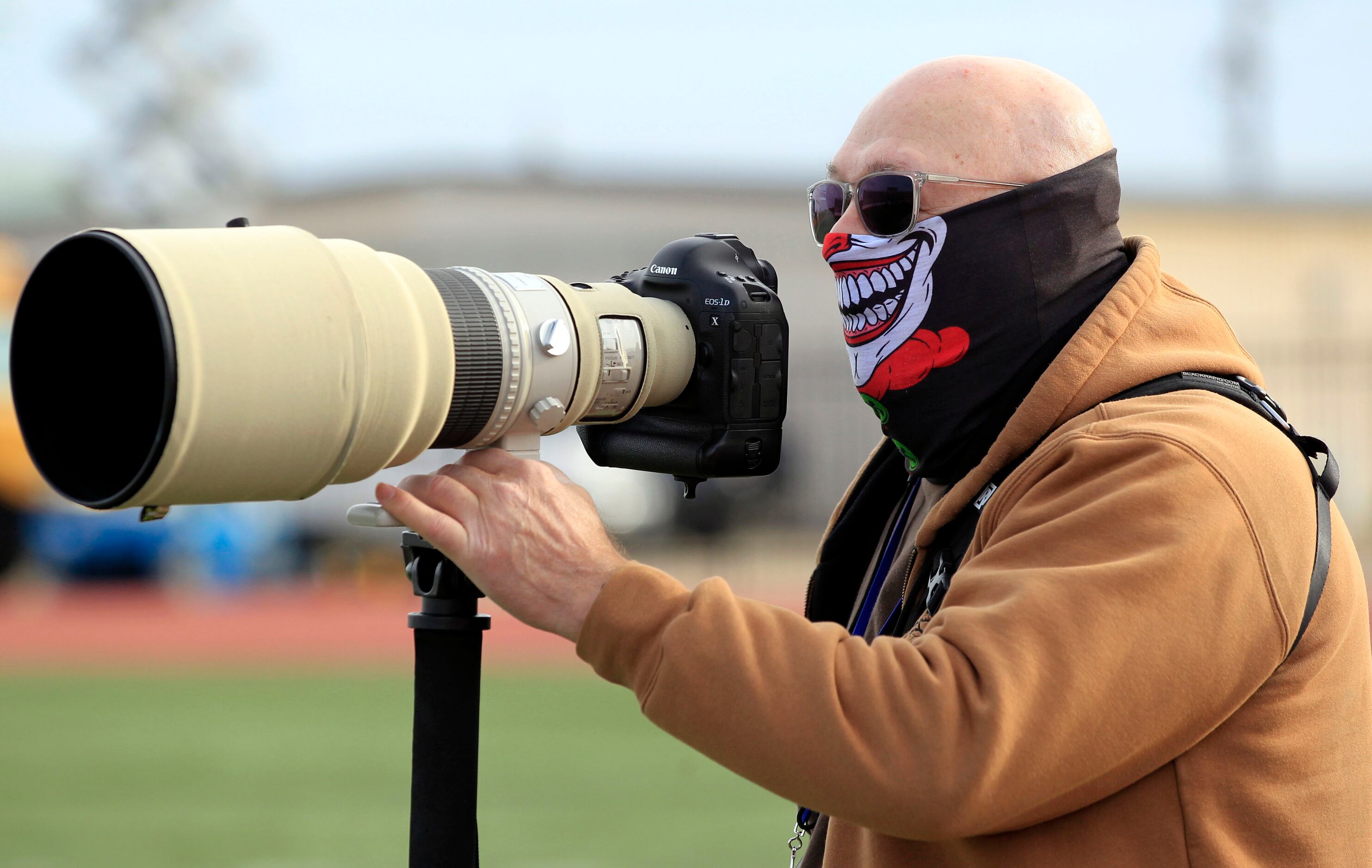 A sideline photographer sports a grinning mask during a high school football game between...