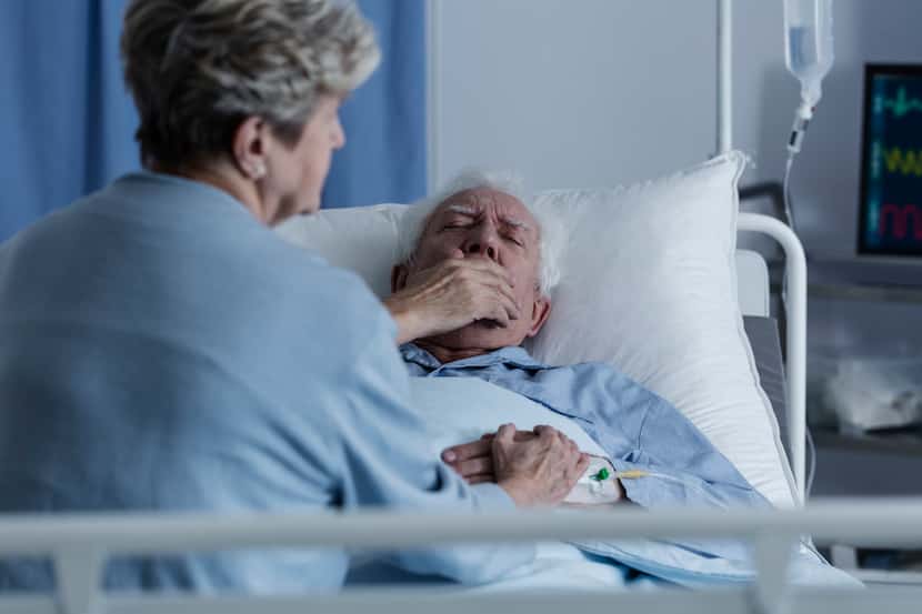 Foto de un hombre en un hospital, tosiendo, y su esposa a su lado.