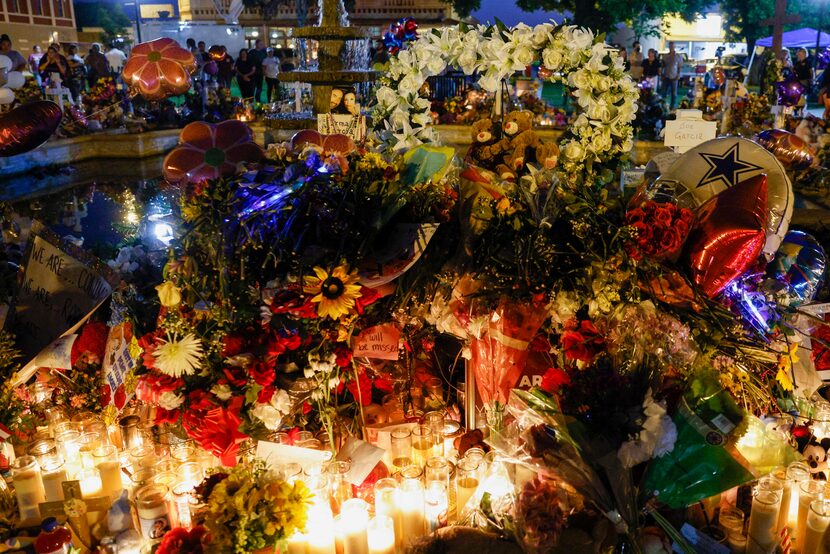 Candles and flowers pile nearly three feet high in front of a  memorial for Robb Elementary...