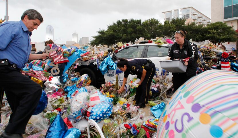 Dallas Police officers and volunteers help pick up items from the memorial at Dallas police...