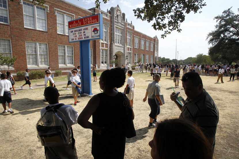 Parents wait for their children under the shade of a large oak tree on the first day of...