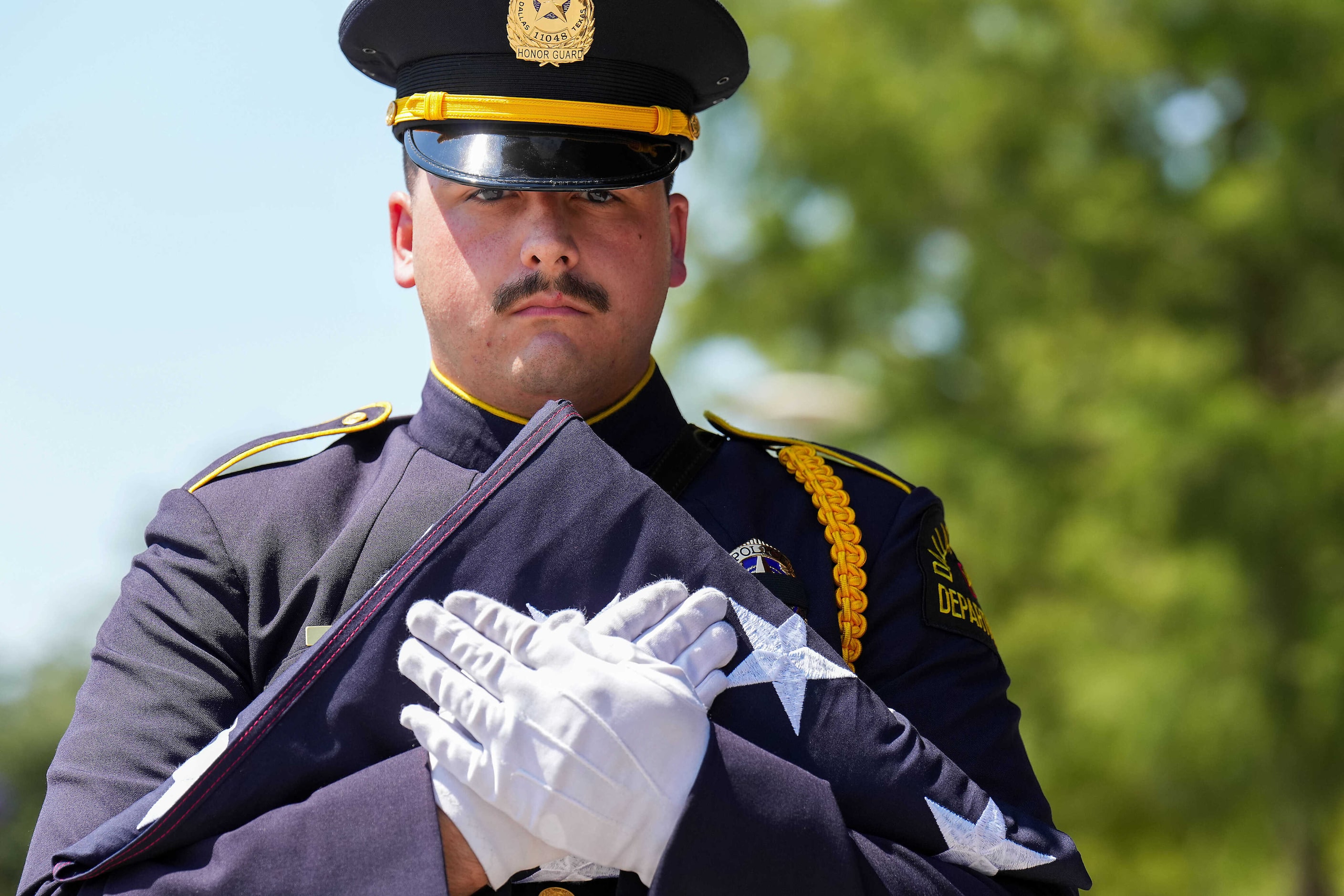 A member of the Dallas Police Honor Guard  carries the folded flag from the casket of...