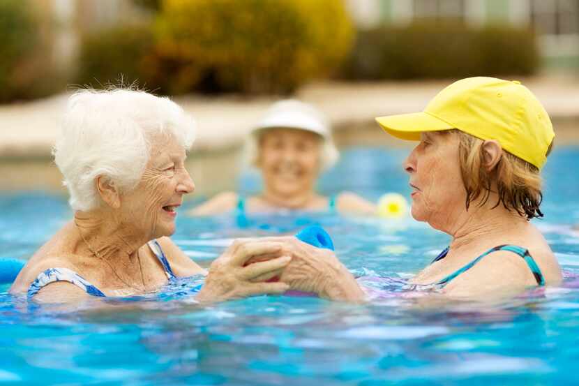 Three older women swim in a pool while smiling.