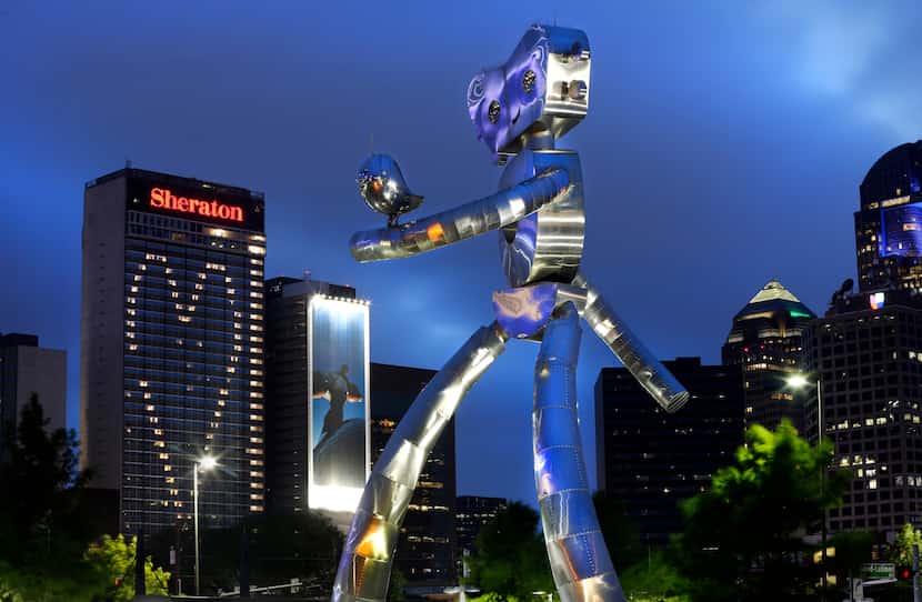 The Dallas skyline twinkles behind one of the "Traveling Man" sculptures that serve as Deep...