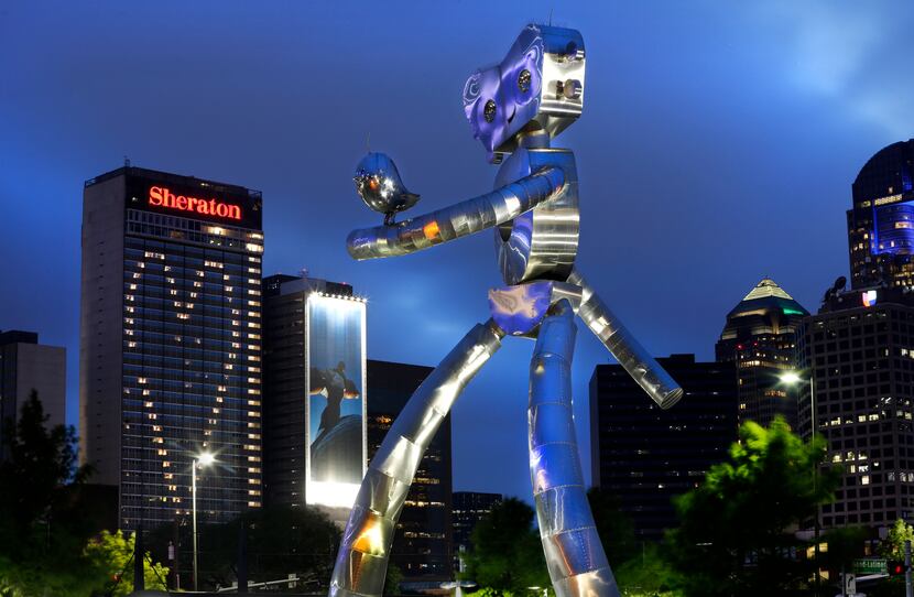 The Dallas skyline twinkles behind one of the "Traveling Man" sculptures that serve as Deep...