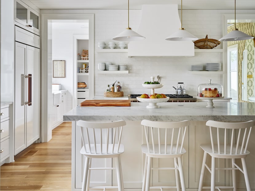 A kitchen has counter-height stools at the countertop, open shelving near the stove and...