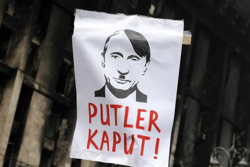 A man holds a sign depicting Russian President Vladimir Putin as World War II German...