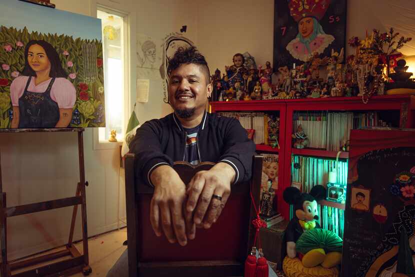 Smiling man sits in a living room in front of artworks he has created.