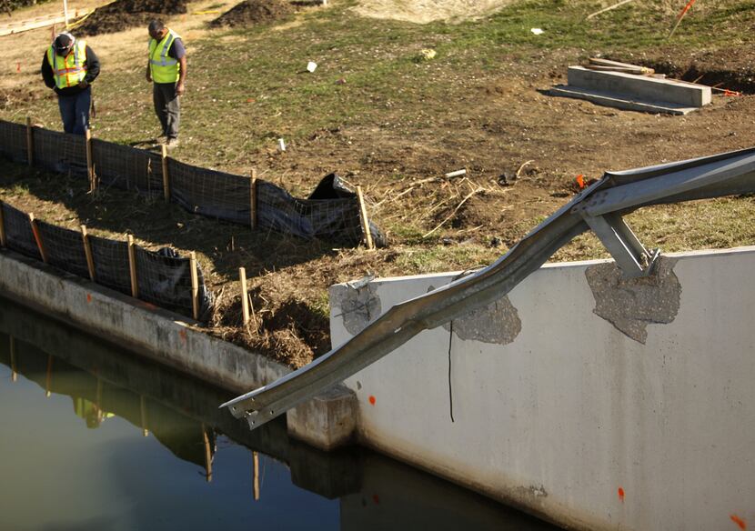 A pair of workers inspect the damage to a protective guardrail along a roadside canal in...
