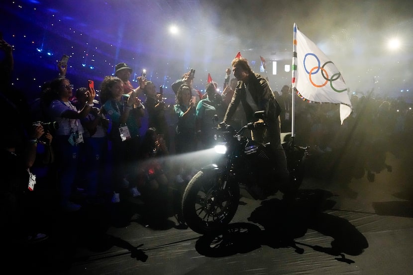 Tom Cruise monta una motocicleta con la bandera olímpica durante la ceremonia de clausura de...