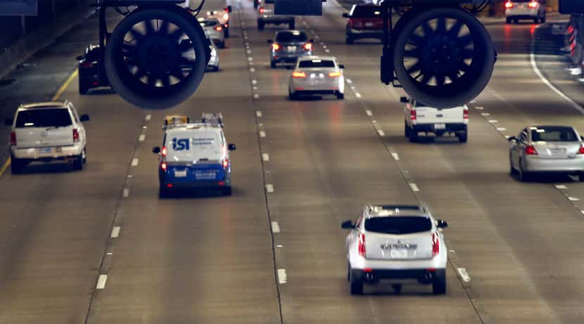 Vehicles on Woodall Rodgers Freeway pass under Klyde Warren Park where large fans are hung...