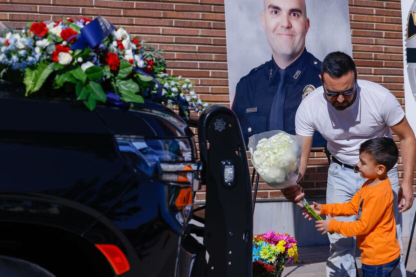 Miguel Gauna helped son Andrew, 5, place flowers on the police car outside of the Carrollton...