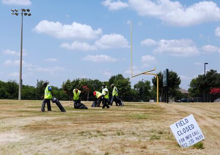 City of DeSoto contract workers roam a football field looking for small debris from a...