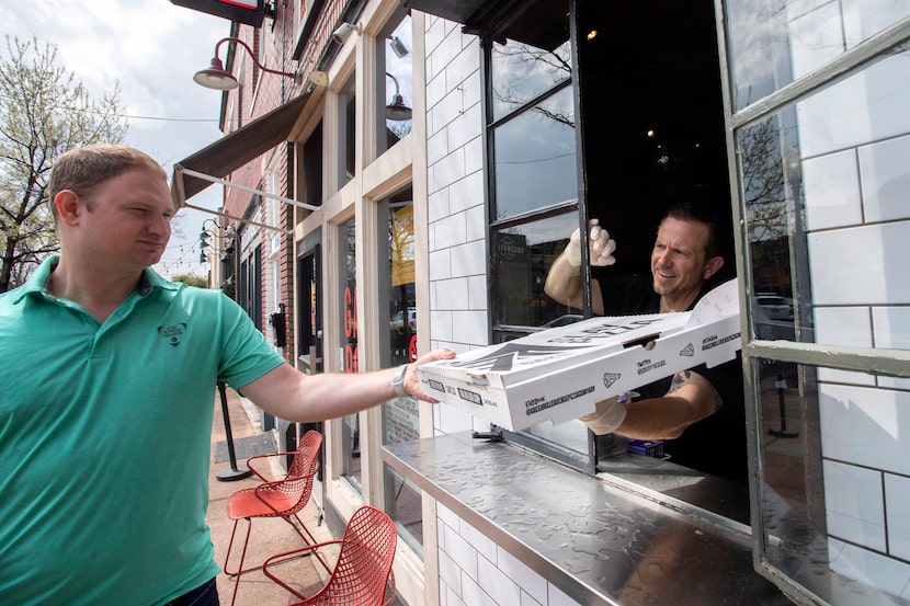 Shelby Wolf, general manager of Greenville Avenue Pizza Company, hands a pick-up order out...