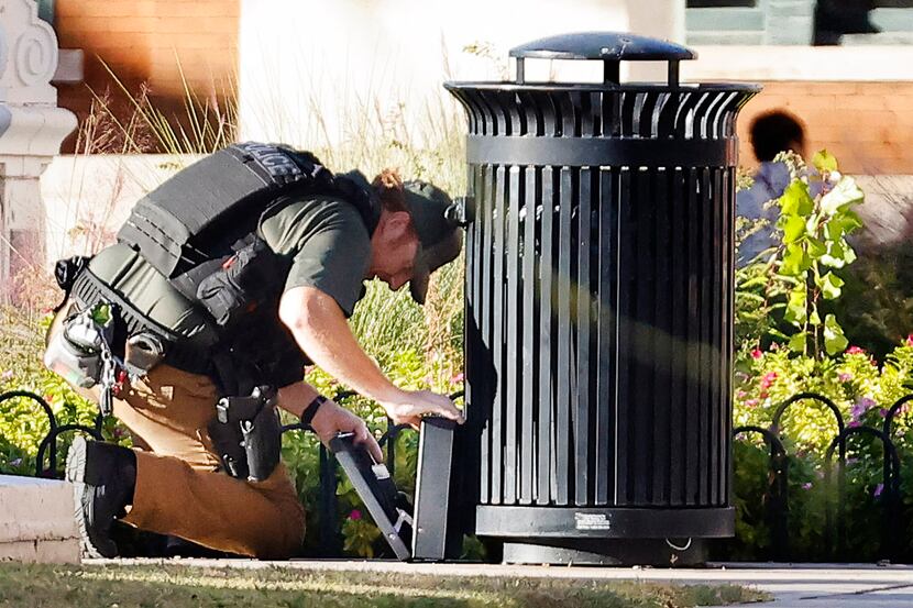A member of the Dallas Police explosive ordnance unit inspects a briefcase left near a trash...