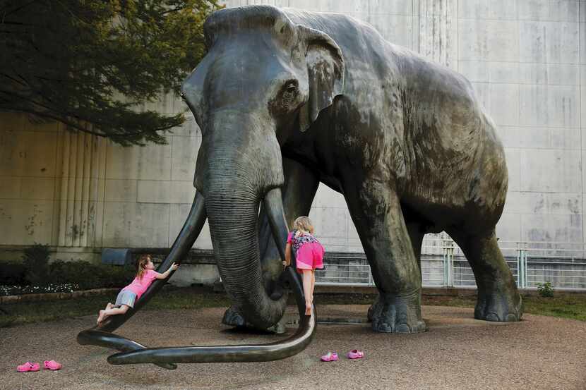 Erin (left), 3, and her sister Ella, 5, of Waxahachie climb on an elephant statue outside...