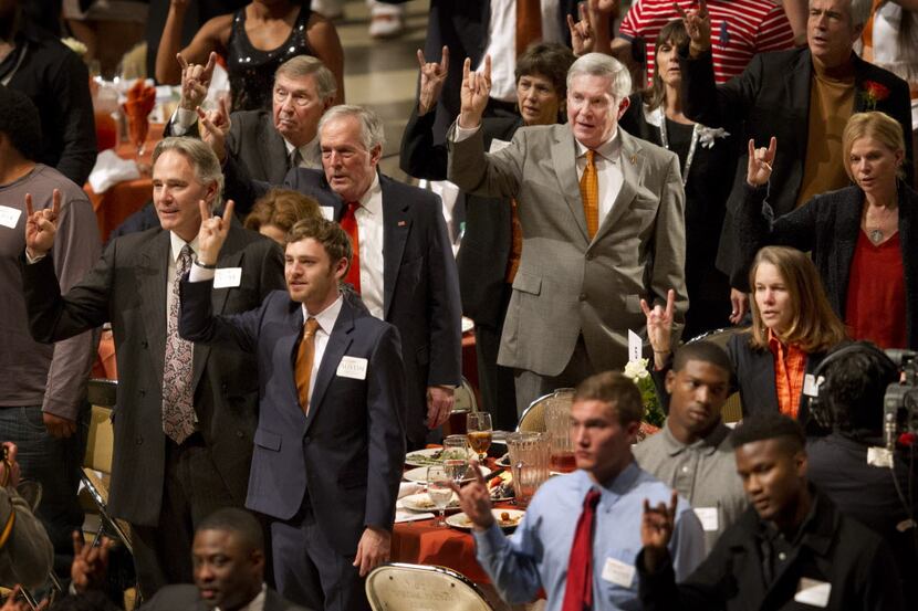 Texas football coach Mack Brown, right in gray suit, stands for the school song during the...