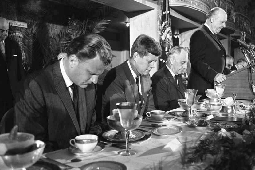 President John F. Kennedy and others at the head table bow their heads during the invocation...