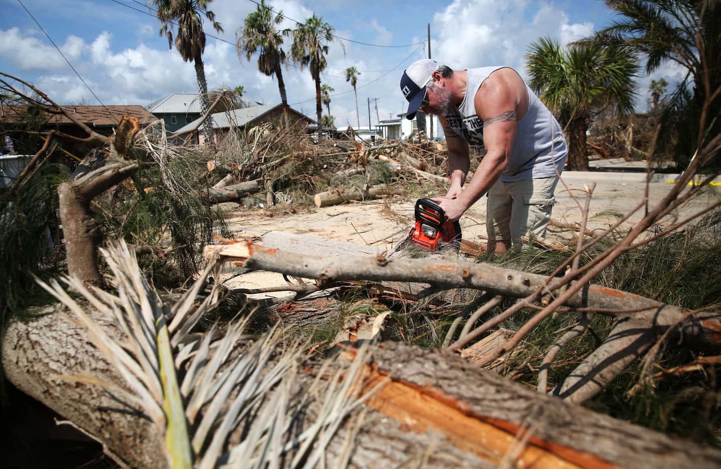 Volunteer Woodie Castaneres of San Antonio uses a chain saw on a fallen palm tree outside...