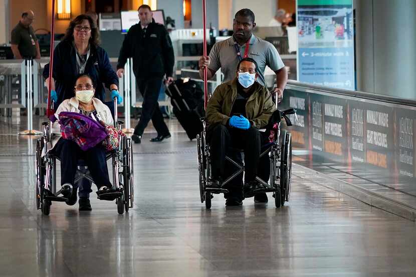 Wheelchair passengers wearing face masks are helped to gates after passing security at Hobby...